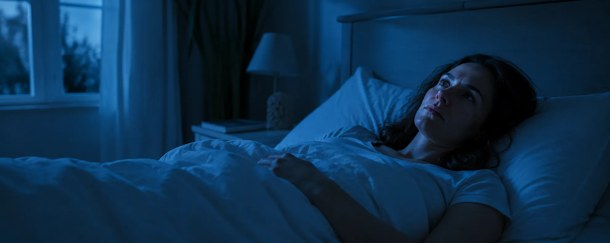 Frau liegt nachts wach im Bett und blickt grübelnd zur Decke – Symbolbild Schlaflosigkeit und Einschlafprobleme, Hypnose zur Schlafverbesserung in Augsburg